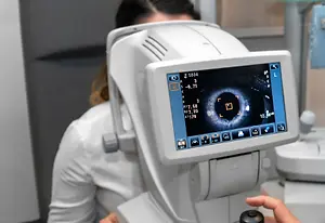 A woman is having her eye examined by a man in an eye clinic with a monitor showing results