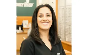 A woman in a black shirt is smiling and posing for a photo in an optical shop.