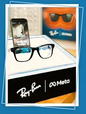 A black and white box with a pair of Ray-Ban glasses on top, a smartphone with the text 'TRY ON THE GLASSES' and a Ray-Ban box in the background.