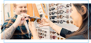 A man holding glasses while a woman holds them up to his face at a sunglass store