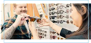 A man holding glasses while a woman holds them up to his face at a sunglass store