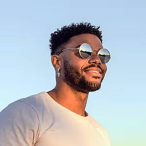A smiling black man in sunglasses and a white shirt poses for a picture.