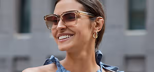 Smiling woman with glasses and blue dress standing in front of buildings