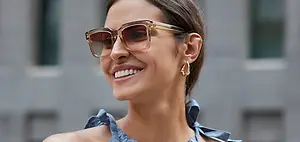 Smiling woman with glasses and blue dress standing in front of buildings