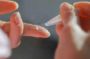 A person is holding a transparent lens in their hand and probably applying it to their eye.