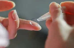 A person is holding a transparent lens in their hand and probably applying it to their eye.