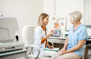 A woman in a blue shirt talks to an eye doctor in a white coat about her vision in a medical office