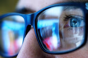 A close-up of a person's eye with blue-tinted glasses.