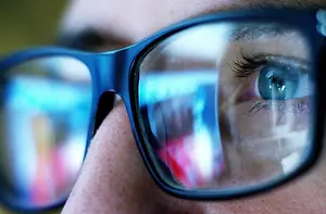 A close-up of a person's eye with blue-tinted glasses.