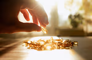 A hand holds a golden-colored capsule in front of a cluster of similar capsules on a table.