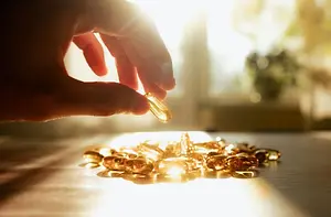 A hand holds a golden-colored capsule in front of a cluster of similar capsules on a table.
