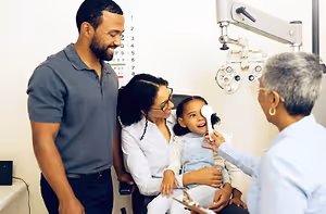 An adult woman holds a young girl for an eye exam at an optometrist's office