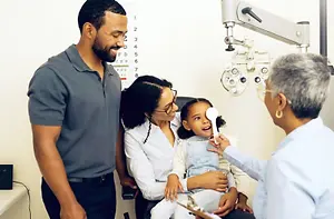 An adult woman holds a young girl for an eye exam at an optometrist's office