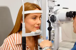 A woman is getting an eye exam in a clinic with an optometrist using a microscope to check her eyes