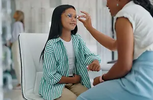 A young girl is trying on glasses in a store while a woman holds her glasses to her eyes.