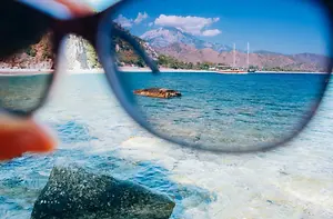 A pair of glasses showing a view of a beach with rocks, water, and mountains in the distance.