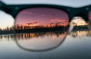 A pair of sunglasses reflecting a sunset over a body of water with trees in the background