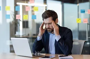 A man in a business suit is sitting at a desk with his hand on his head.