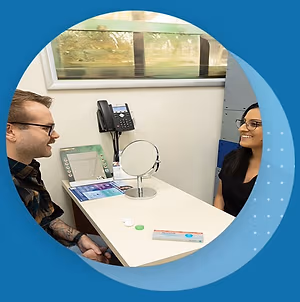 A man and a woman are sitting at a desk with a phone and mirror on it.