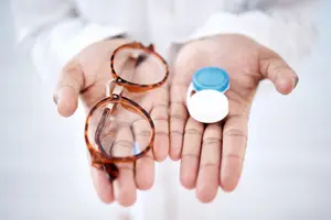An eye doctor holds a pair of glasses and a container of contact lenses.