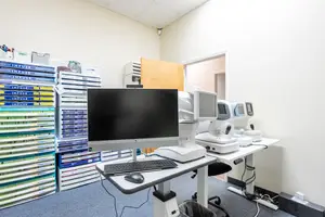 A room with medical equipment, including a monitor and an eye exam machine on a table, and a cabinet with folders and files on the wall.
