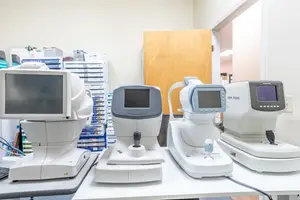 Four white ophthalmoscope machines on a table in a room with a wooden door and shelves in the background