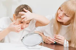 young girl looking in a mirror inserting a contact lens into her eye and a woman sitting next to her