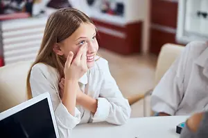 Girl smiling while covering her eye with her hand and talking to someone