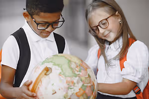 A young boy and girl are looking at a globe in a school hallway