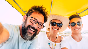 A smiling man, woman, and boy wearing glasses and hats under a yellow canopy.