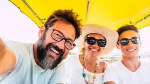 A smiling man, woman, and boy wearing glasses and hats under a yellow canopy.