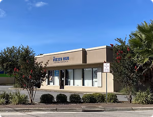 A building with the words 'The Vision Hub' and 'Fort Walton Beach' on it, surrounded by plants and trees.