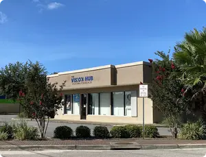 A building with the words 'The Vision Hub' and 'Fort Walton Beach' on it, surrounded by plants and trees.