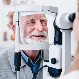 An older man with a white beard looks into an eye exam machine while smiling
