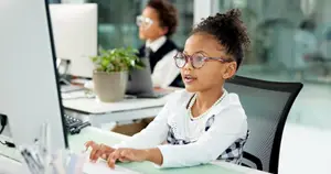 A young girl with glasses sitting at a desk using a computer