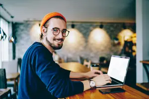 A man sitting at a table using a laptop and smiling