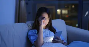 Woman sitting on a couch, looking at her phone, and holding her nose while looking upset