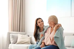 Two women sitting on a couch and smiling, one with her arm around the other