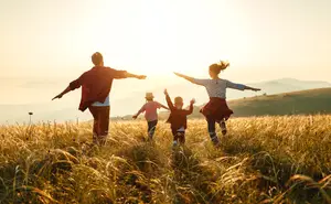 A family of four people running together on a grassy field