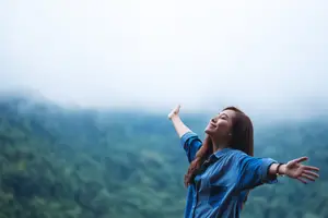 A woman with her arms raised and smiling while standing on a mountain in the fog