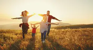 A family of four is joyfully running together in a field at sunset