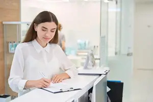 A woman sits at a desk writing on a notepad in a modern office