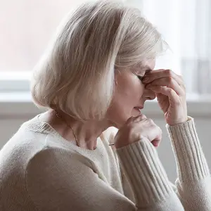 Close-up of an elderly woman sitting and looking pensive with her hand on her face