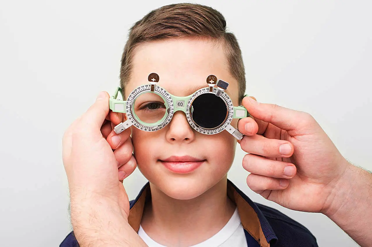 A boy wearing trial frame spectacles and holding them up to his face