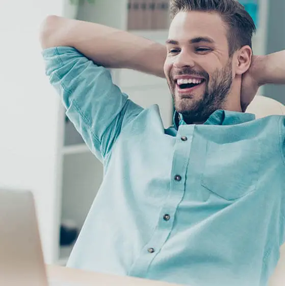 Man smiling and leaning back in chair with laptop on desk
