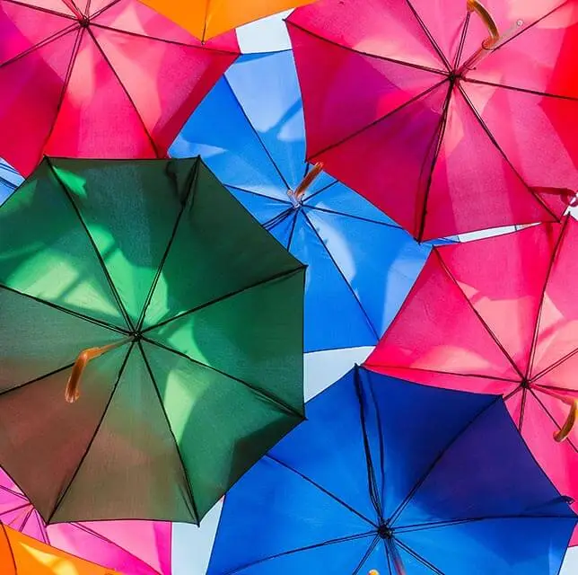 An array of multi-colored umbrellas including green, pink, orange, blue, and red, displayed against a blue sky background.