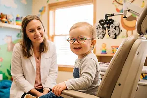 A woman in a white coat is examining a baby's teeth while sitting in a dentist's chair.