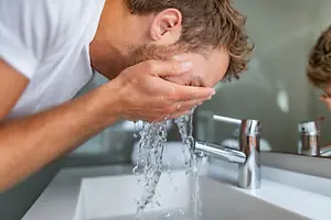Man washing his face with water in front of a sink