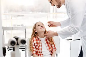 A young girl is smiling and having her eyes checked by a male doctor in a clinic.