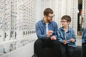 A man with glasses and a boy sitting in front of a wall of glasses